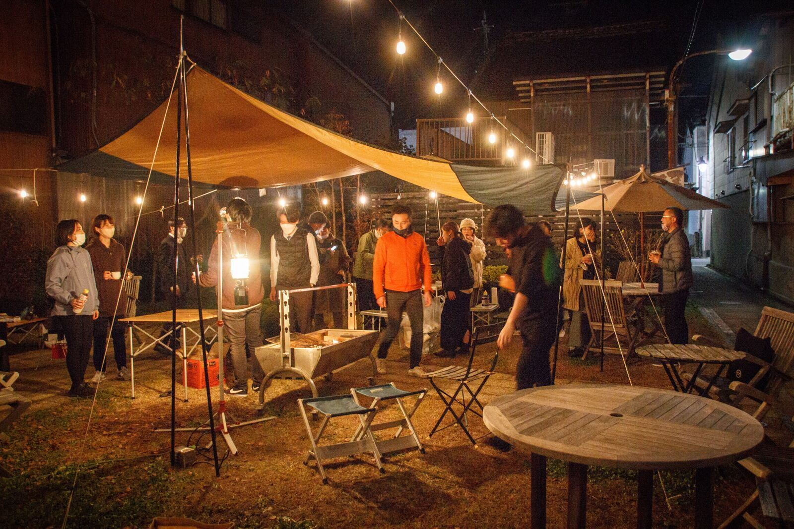 夜の屋外、タープと灯りの下に集まる人たち